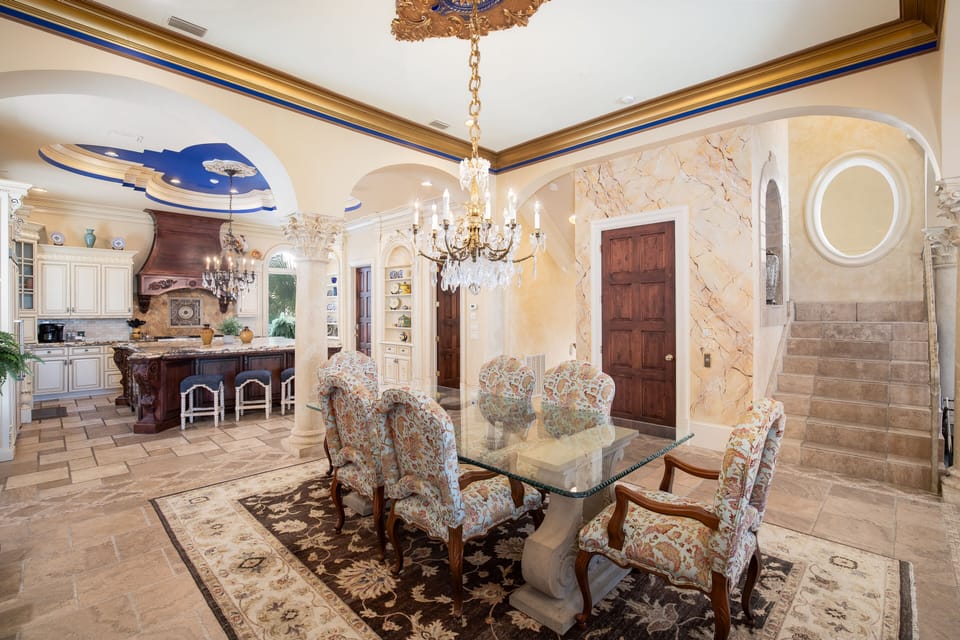 Step into your palatial dining space where ornate chandeliers cast warm light over elegant furnishings and artistic ceiling details.