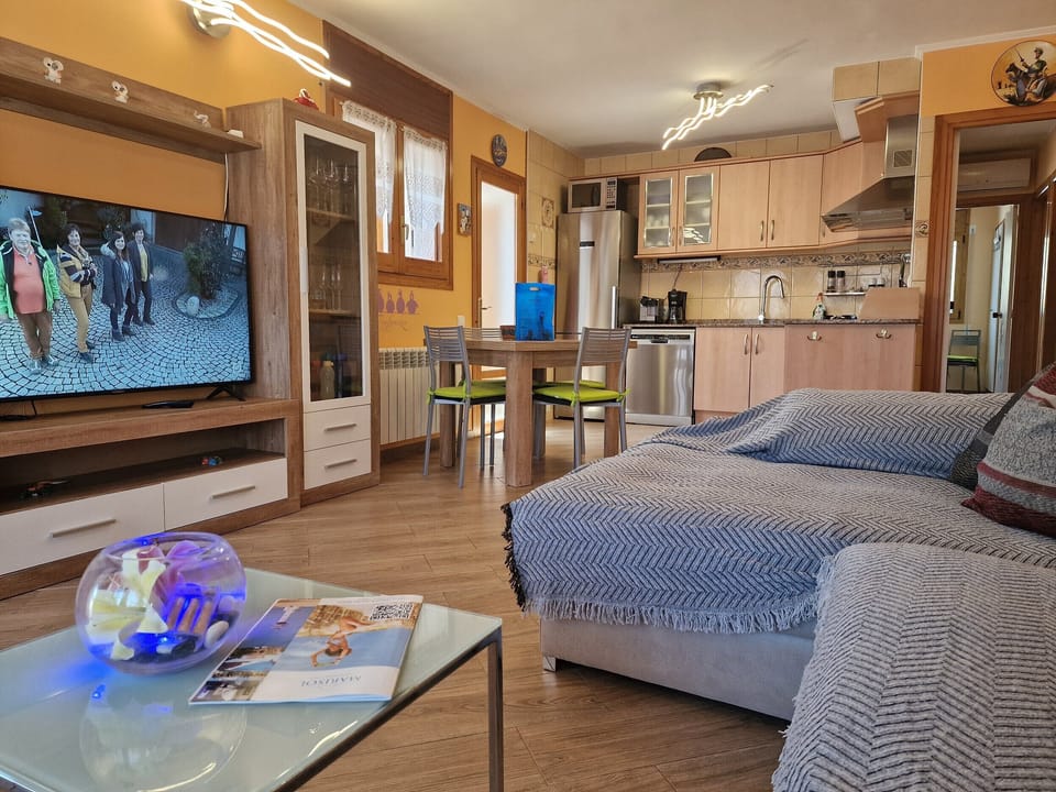 The bright living room of House Don Quichotte features an open-plan layout, a large flat-screen TV, and a seamless transition to the dining area and kitchen.