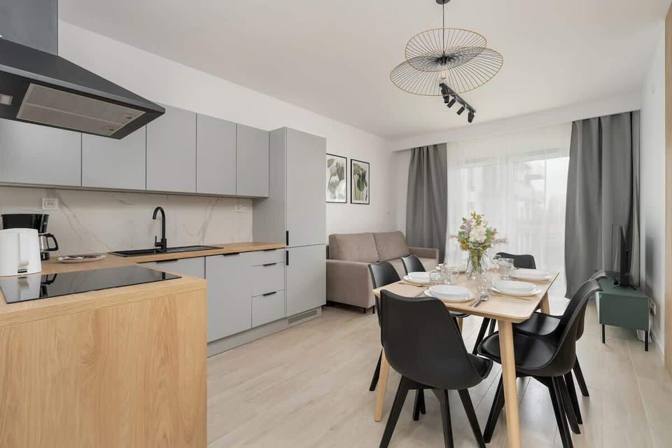 An open-plan kitchen and dining area with white cabinetry, black dining chairs, and a chic pendant light above the table.


