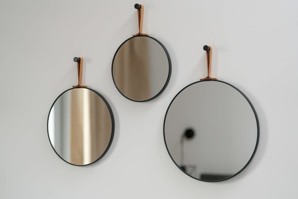 A trio of round mirrors with minimalist leather straps, creating a stylish and artistic wall display.

