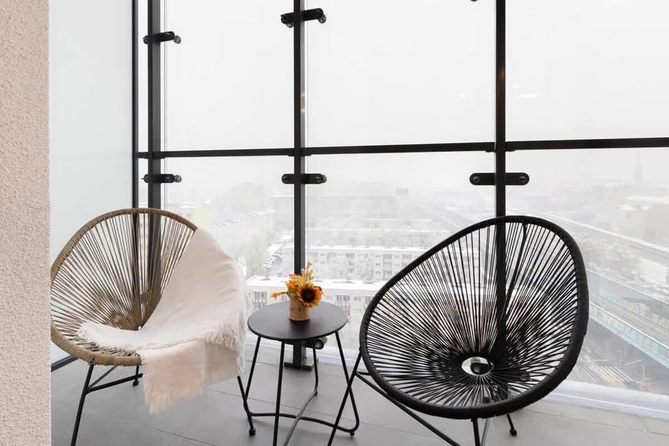 A balcony with chic black wicker chairs and a small coffee table, providing a comfortable outdoor relaxation area with city views.

