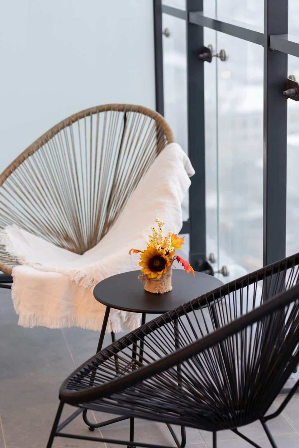 A balcony corner with a stylish rattan chair and small side table, offering a cozy spot to enjoy city views and fresh air.

