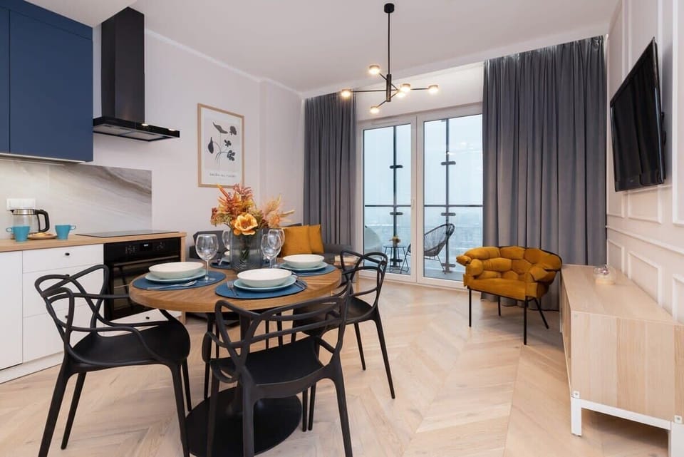 An open-plan dining and kitchen area with a black round table, blue cabinetry, and modern pendant lighting for an elegant dining experience.

