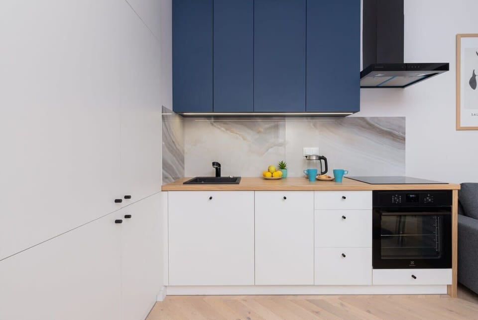 A compact kitchen with blue upper cabinets, white countertops, and modern appliances, maintaining a sleek, minimalist design.

