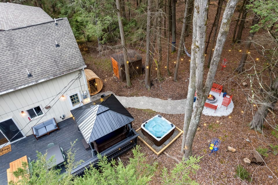 Cozy outdoor retreat surrounded by nature, featuring a hot tub, a fire pit lounge, and a barrel sauna—perfect for relaxing and unwinding in a private wooded setting.