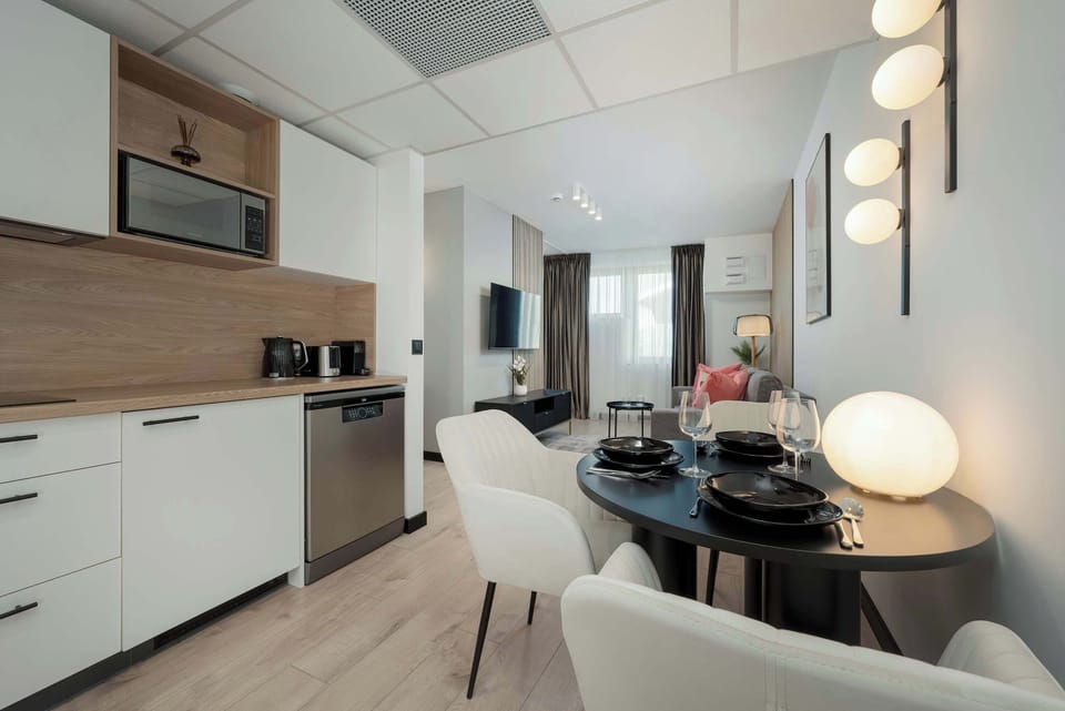 The living room flows into a dining space, with soft neutral tones and a round dining table for four. Art pieces decorate the walls, and the room has a cozy, inviting atmosphere.