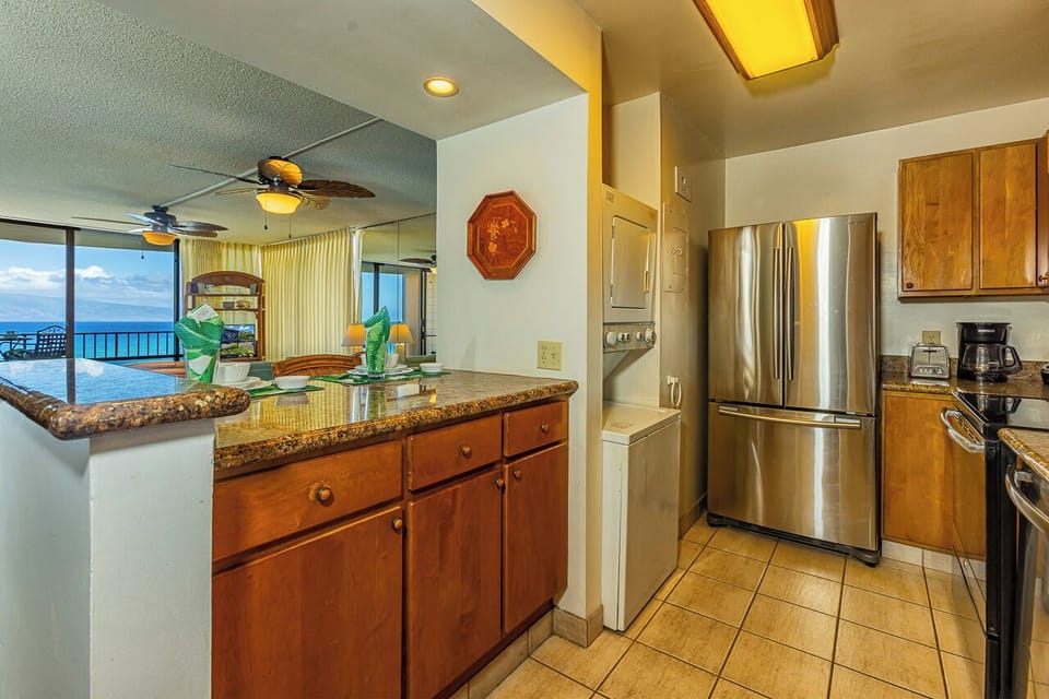 Step into your fully equipped kitchen with stainless steel appliances, warm wood cabinetry, and stunning ocean views that stretch beyond the open living area.