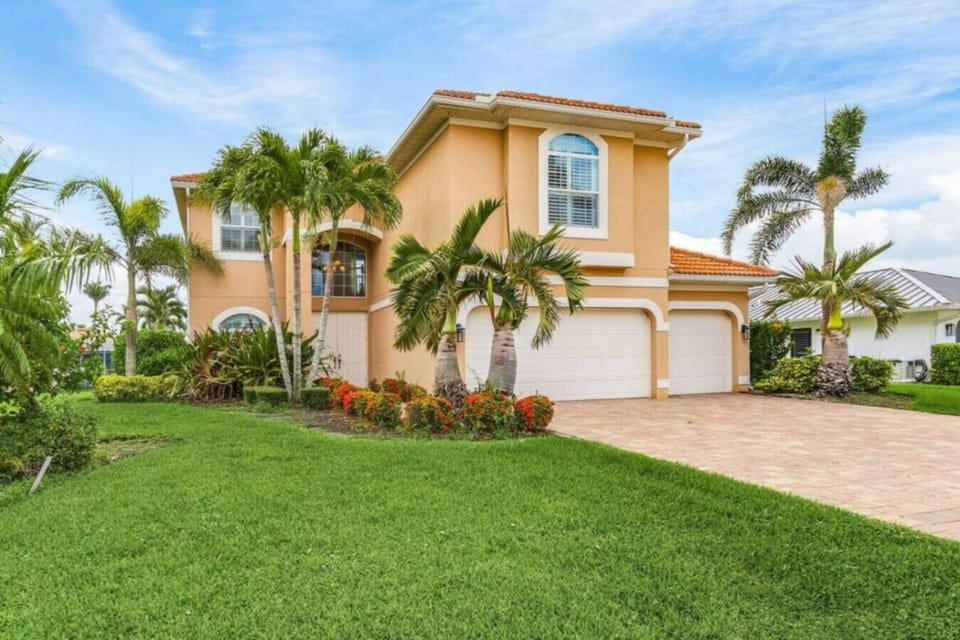 Spacious driveway leading to a tropical villa with lush landscaping.