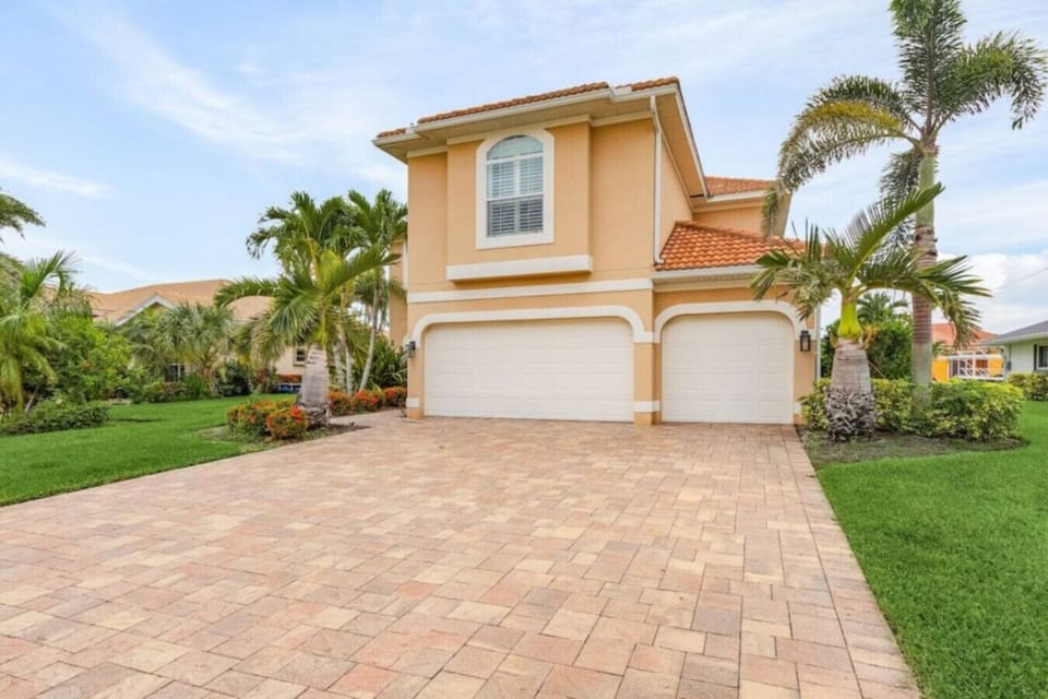 Spacious driveway with tropical landscaping and a three-car garage.