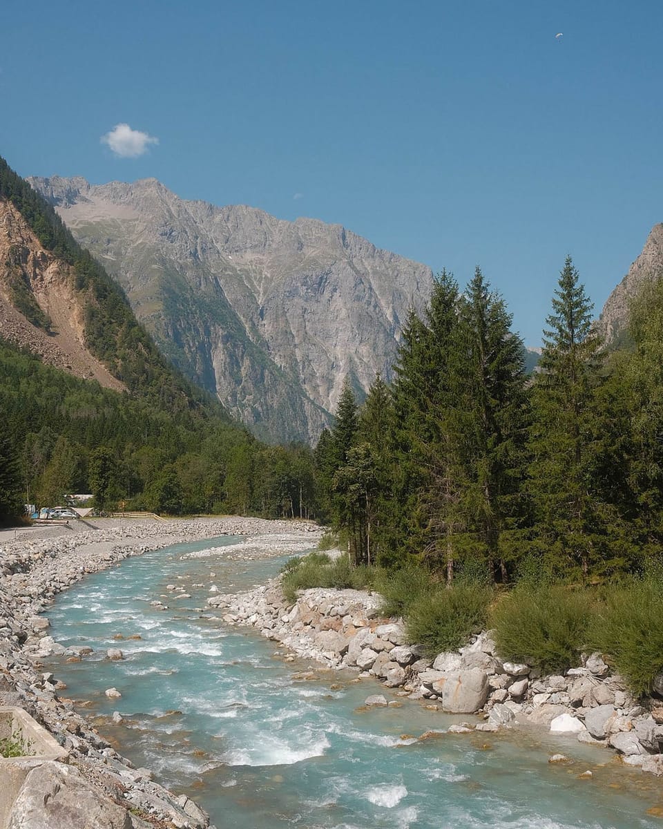 A glacial turquoise river rushes through a rocky Alpine valley beneath the towering peaks of Les Deux Alpes, in the heart of the French Alps.