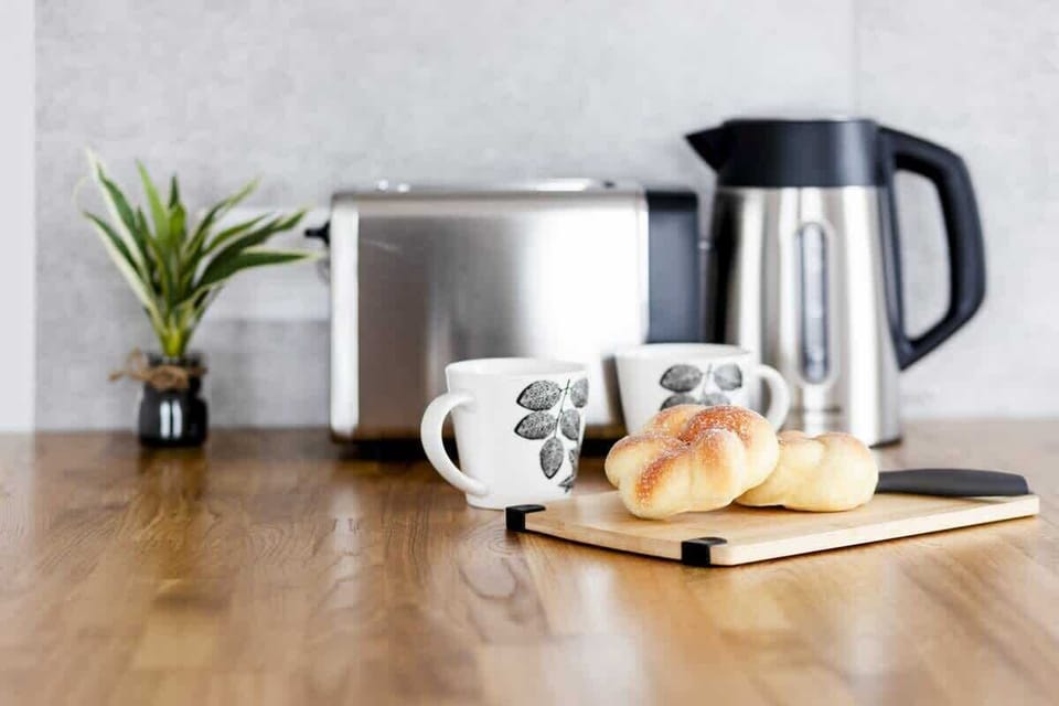 A coffee and tea station with a kettle, cups, and fresh croissants.
