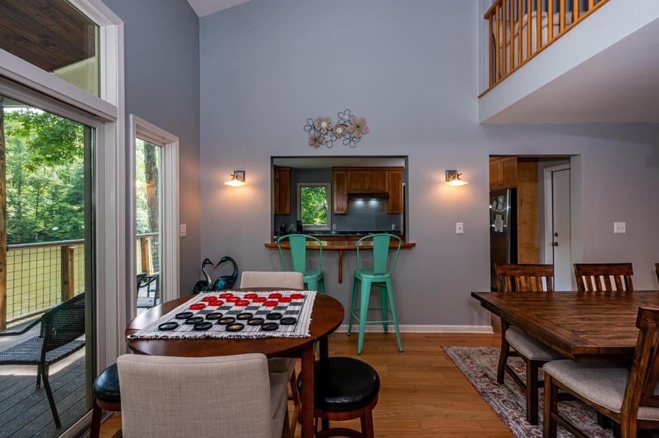 Dining area with round wood table set for checkers game, teal metal bar stools, and sliding glass door to deck.