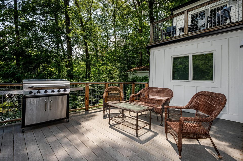 Outdoor deck with gray wood planks, wicker seating set, glass-top coffee table, and stainless steel grill.