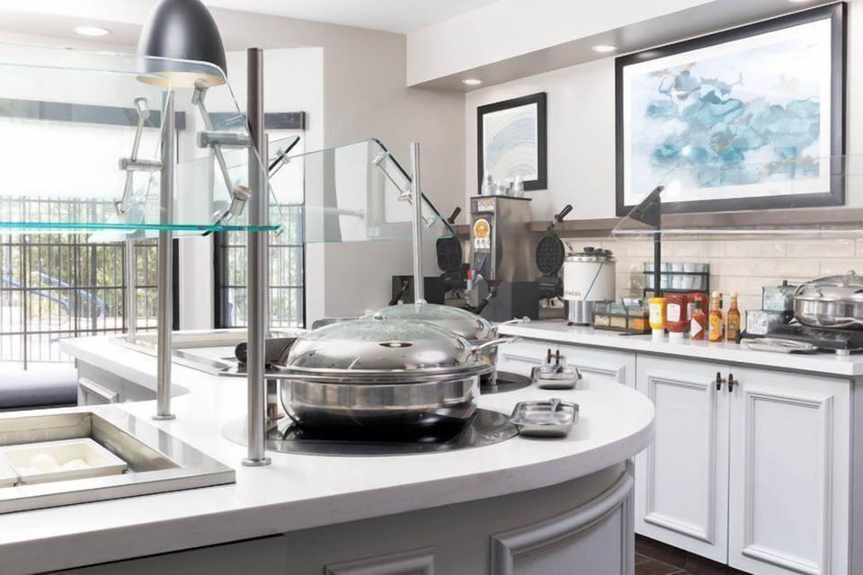 Breakfast service counter with silver chafing dishes, condiments, a coffee machine, and a view of the outdoor seating area