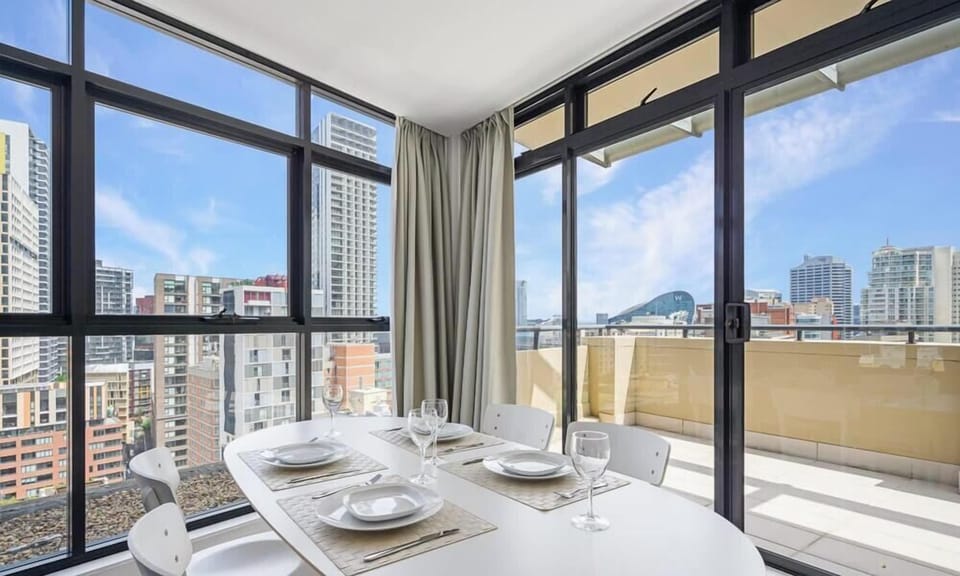 Dining area with table setting and floor-to-ceiling windows leading to the balcony with city views.