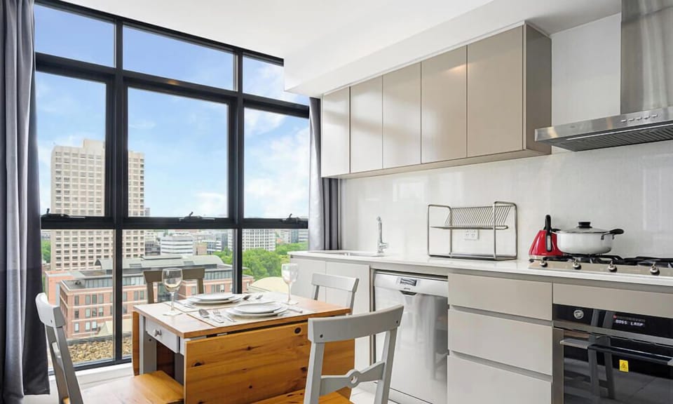 Modern kitchen with window outlook, stone benchtops, cooktop, oven, and dining table nearby.
