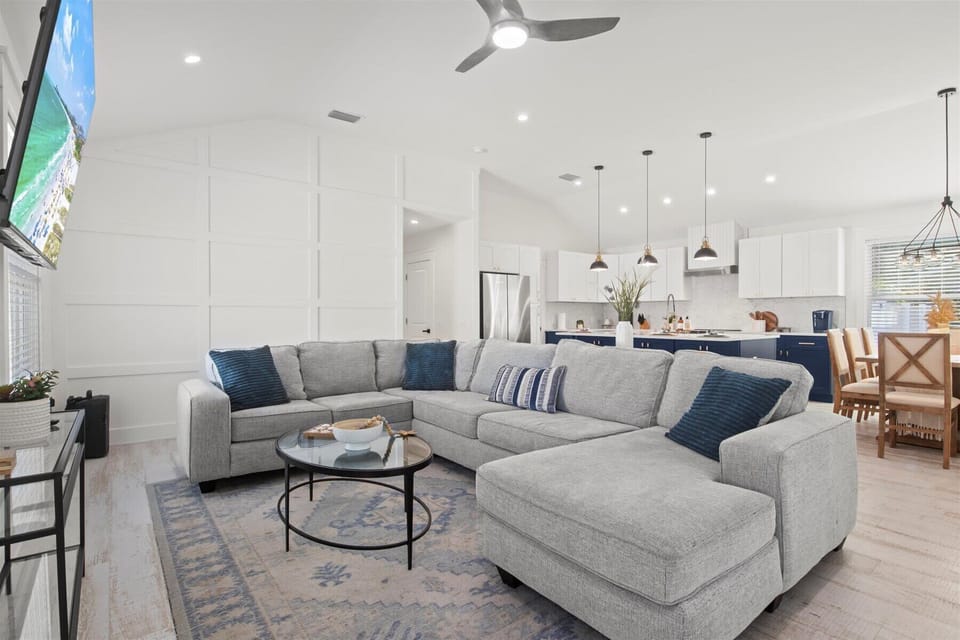Coastal-Inspired Gathering Space: Unwind in this airy, open-concept living room featuring a plush sectional, streaming natural light, and seamless flow to the kitchen—ideal for family bonding and relaxed entertaining.