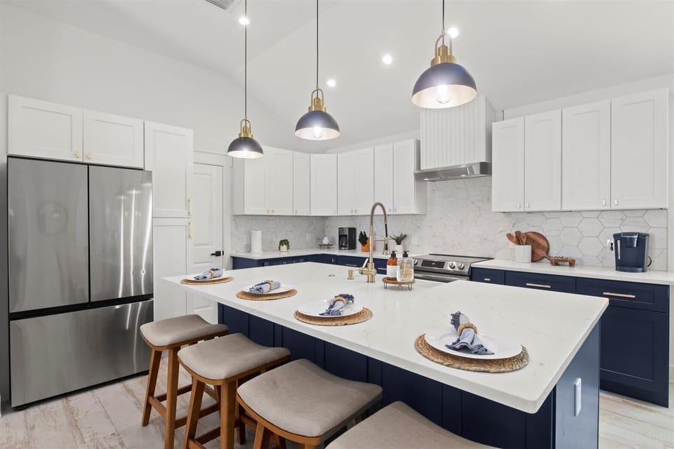 Stylish & Functional (FULLY STOCKED) Kitchen: Experience the perfect blend of modern aesthetics and functionality in this kitchen, featuring white and navy cabinetry, elegant lighting, and thoughtful decor.
