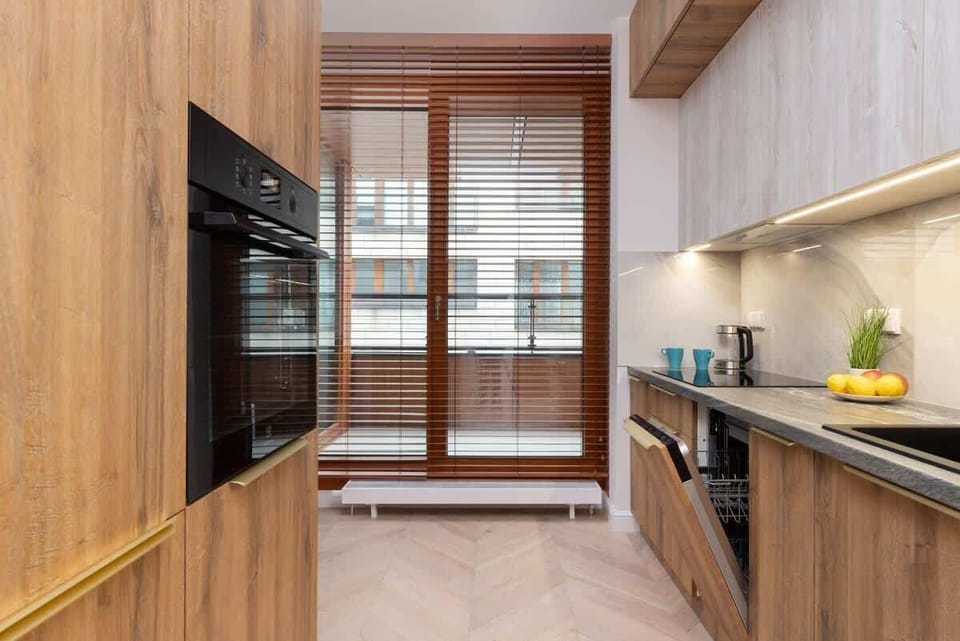A compact kitchen corner with wooden lower cabinets, a marble-inspired backsplash, and a built-in stovetop beneath a shuttered window.

