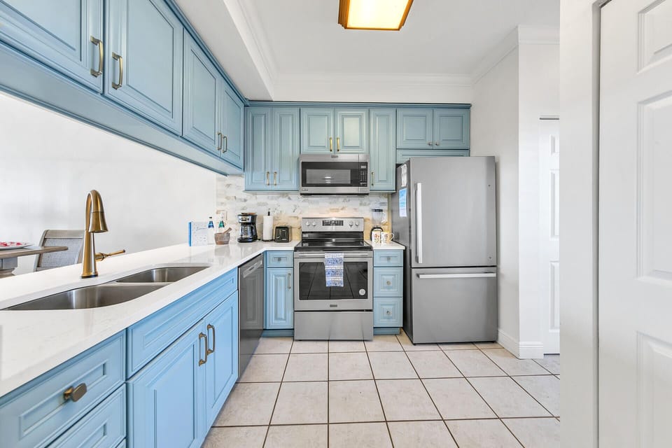 Your beautifully renovated kitchen features elegant blue cabinetry, modern stainless steel appliances, and warm gold accents creating the perfect space for cooking.