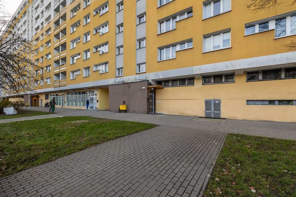 The exterior of a yellow apartment building with paved walkways and green spaces.

