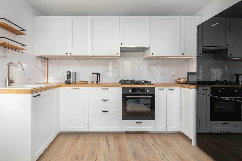A bright kitchen with white cabinets, wooden countertops, and black appliances.

