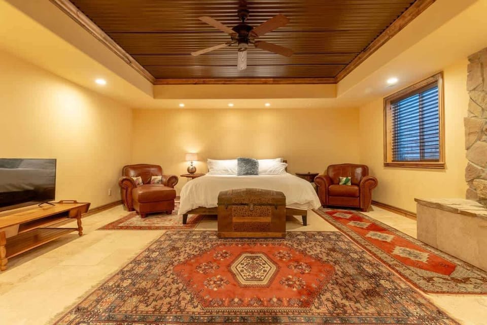 This cozy bedroom with a plush king-sized bed promises restful nights. Enjoy the comfort of leather chairs perfect for unwinding, and the warm glow of ambient lighting that complements the classic wooden furnishings and vibrant area rug.
