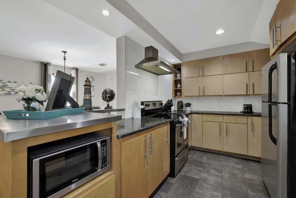 The kitchen is equipped with an electric stove, microwave, refrigerator, toaster, and coffee pot, along with cooking utensils, pots and pans, and dinnerware.