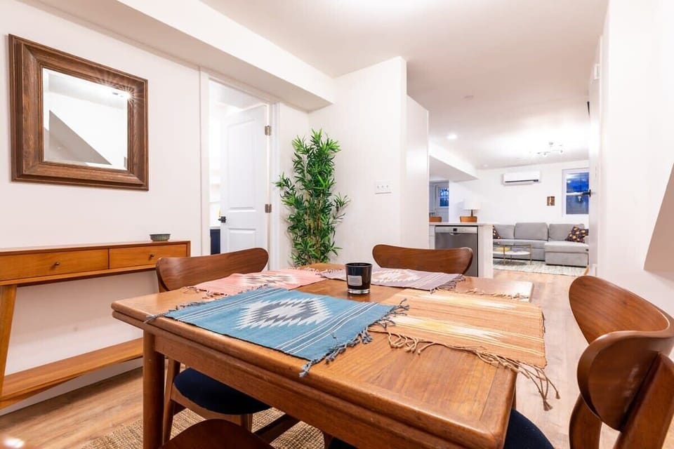 Dining room with seating for four, mirror and decorative plant. In the baclground is the living room. 
