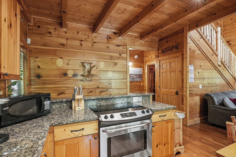 Your cozy cabin features a fully-equipped kitchen with granite countertops, modern appliances, and warm wood walls inviting you to feel right at home.