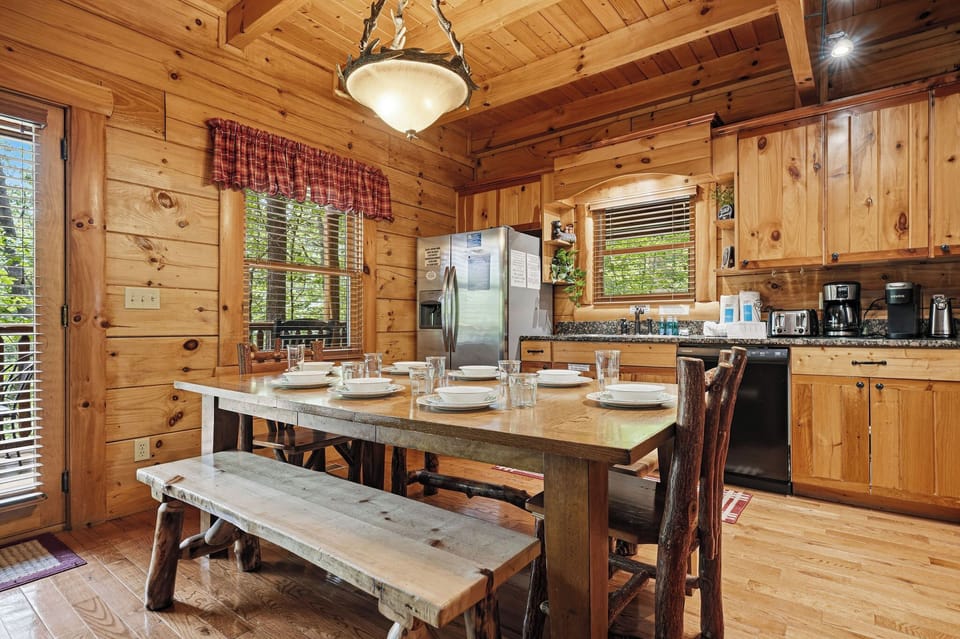 Gather around the handcrafted dining table in your fully equipped cabin kitchen, where rustic wood beams and warm pine walls create a cozy mountain retreat perfect for sharing meals with family and friends.
