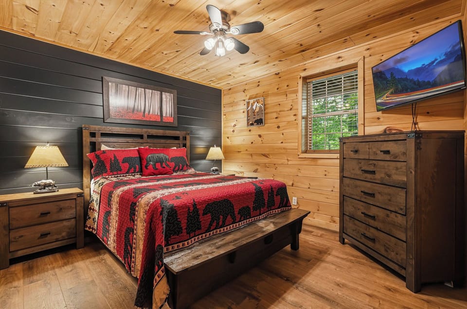 Your cozy cabin bedroom blends rustic pine walls with stylish black shiplap, creating a warm retreat where you'll drift off under the glow of bedside lamps and a ceiling fan.
