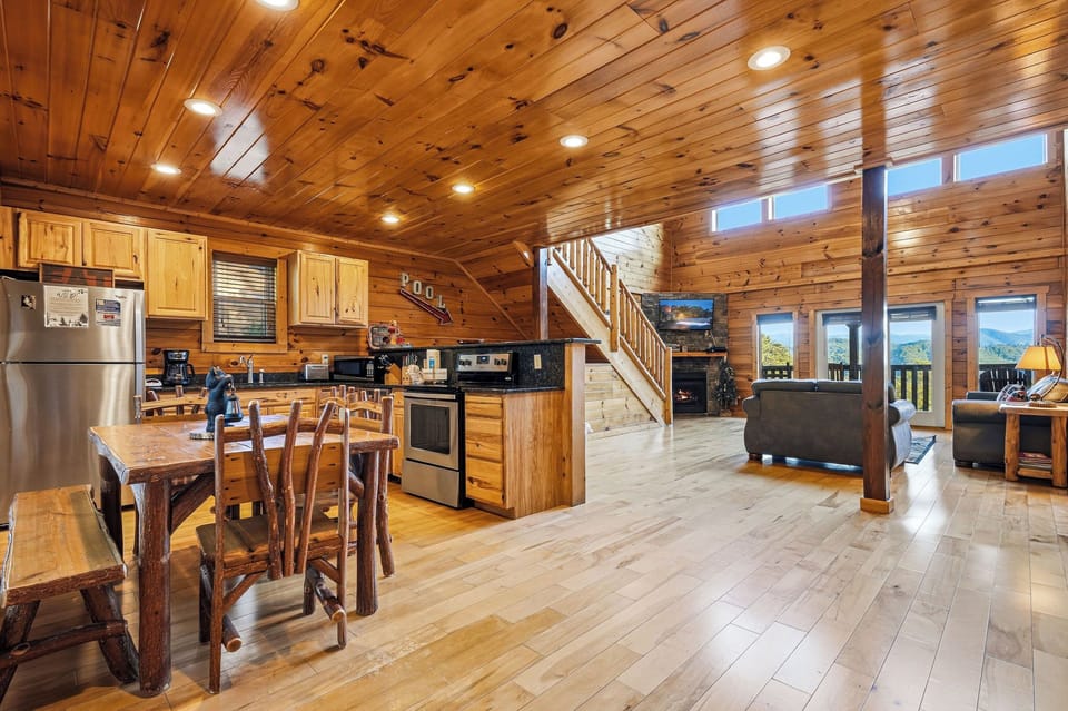 Rustic wood-paneled ceiling and walls create your cozy mountain retreat, where open-concept living flows seamlessly from modern kitchen to comfortable lounge with stunning views beyond the windows.