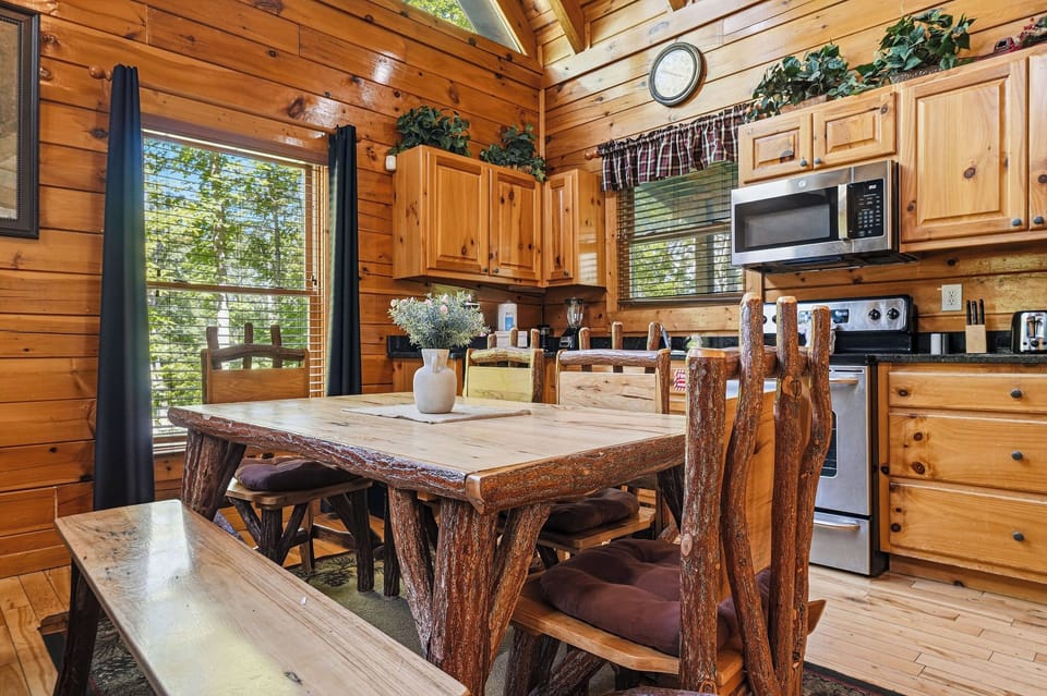 Gather around this handcrafted log dining table where rustic charm meets modern convenience. Your fully-equipped kitchen awaits with all the comforts of home, framed by warm wood and forest views.