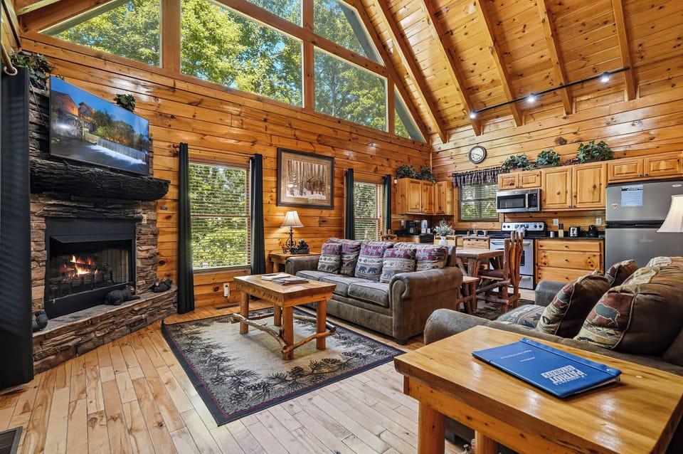 Relax in your open-concept living space with vaulted ceilings, warm wood finishes, and a cozy stone fireplace. Sunlight pours through floor-to-ceiling windows, blending comfort with nature's beauty.