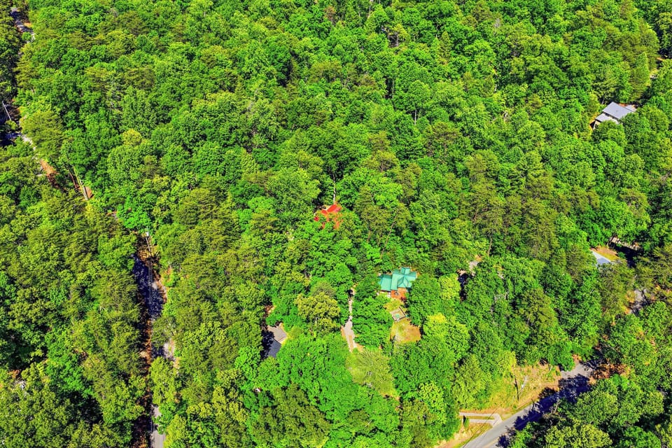 An aerial view showcasing the vacation rental property nestled within lush, vibrant forest, offering guests a secluded and nature-immersed retreat with winding paths and colorful rooftops peeking through the greenery.