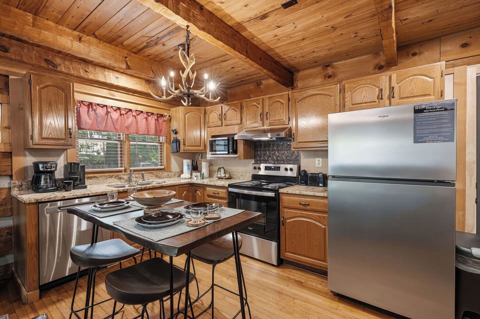 Warm wood beams and golden cabinetry frame your fully equipped kitchen, where modern appliances and granite countertops make meal prep effortless. The island seating invites casual dining under rustic chandelier light.