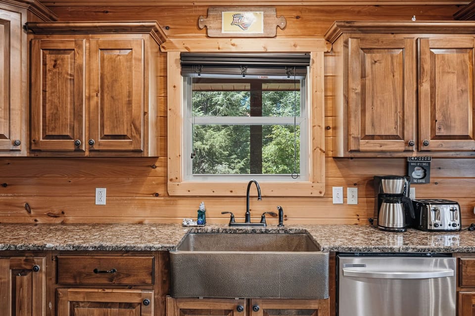 Prepare your favorite meals in a warm, rustic kitchen with modern comforts—farmhouse sink, granite countertops, coffee maker, and a peaceful garden view to inspire your mornings.