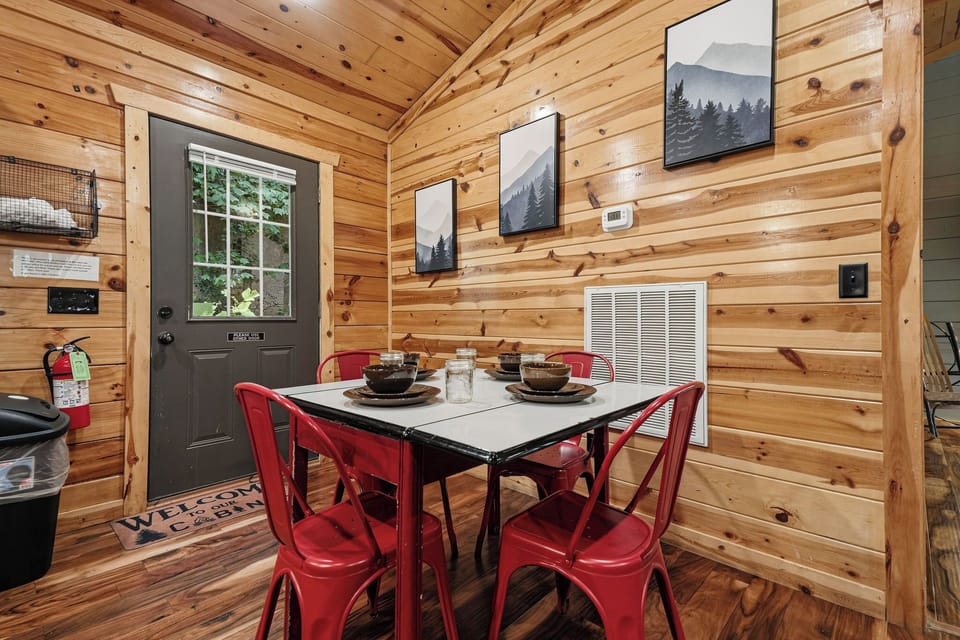 Gather around the inviting dining table in your cozy cabin, where warm wood walls and bright red chairs create the perfect setting for shared meals and great conversation.