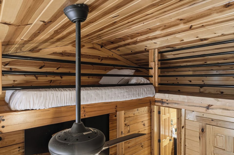 Cozy loft sleeping space with rustic wood-paneled walls and ceiling, featuring a snug bunk setup perfect for peaceful nights in your mountain retreat.