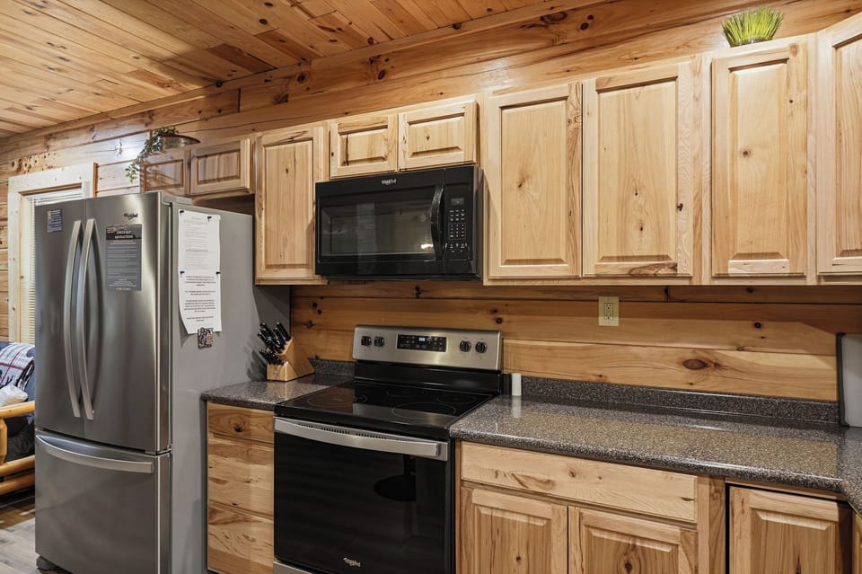 Your fully equipped kitchen features modern stainless-steel appliances, granite countertops, and warm knotty pine cabinetry throughout—perfect for preparing family meals in a cozy mountain retreat setting.