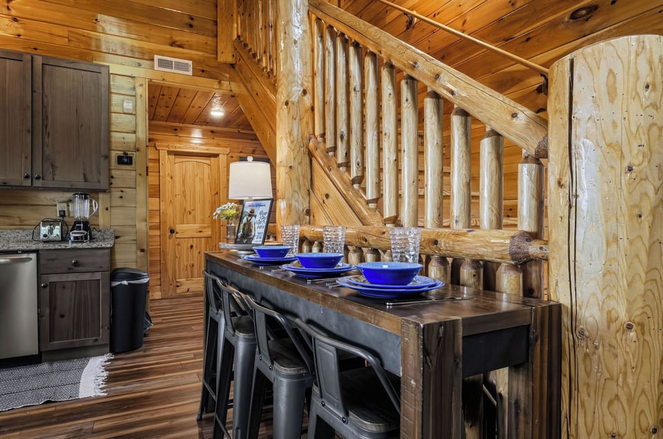 Step inside your rustic cabin retreat where natural wood beams and a stunning log staircase create mountain charm. Your dining area awaits with vibrant blue accents and cozy seating for memorable meals together.