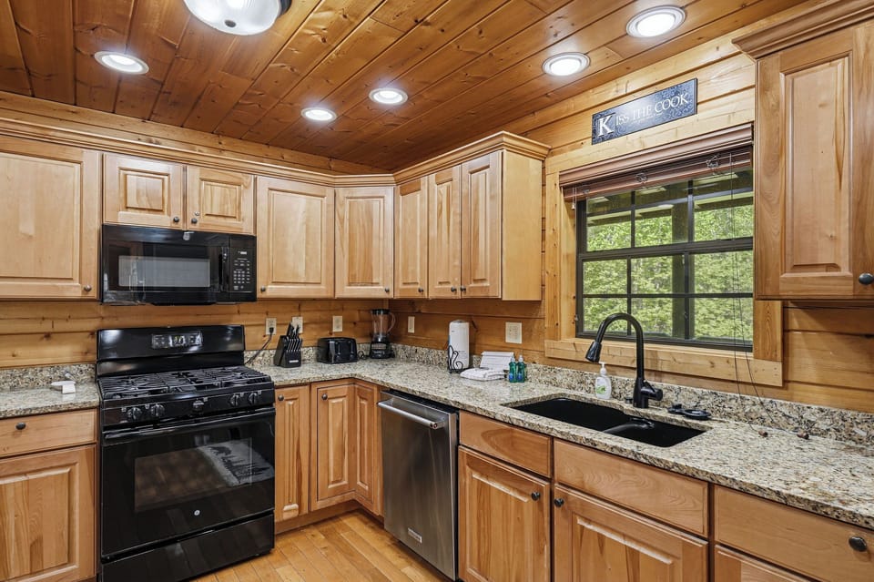 Your fully equipped kitchen features granite counters, gas stove, and dishwasher - perfect for preparing meals while enjoying forest views.
