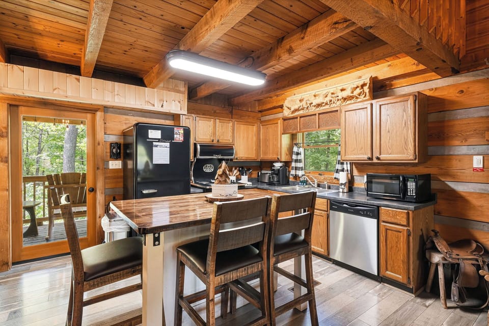 Step into your fully equipped cabin kitchen with warm wood beams, modern appliances, and a charming island where you can share meals with forest views just beyond the door.