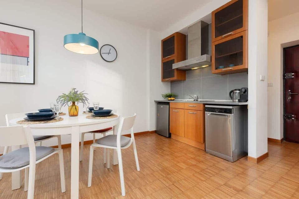 A dining space with a round white table, wooden cabinets, and a wall clock, creating a cozy eating area.

