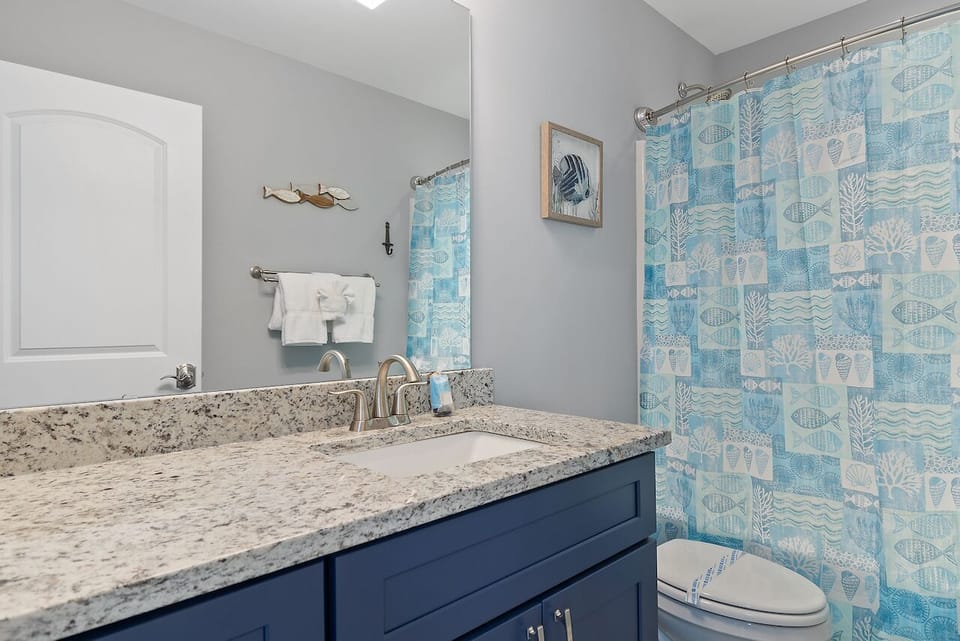 Refresh in your coastal-themed bathroom with granite counters, navy vanity, and cheerful ocean-inspired shower curtain.