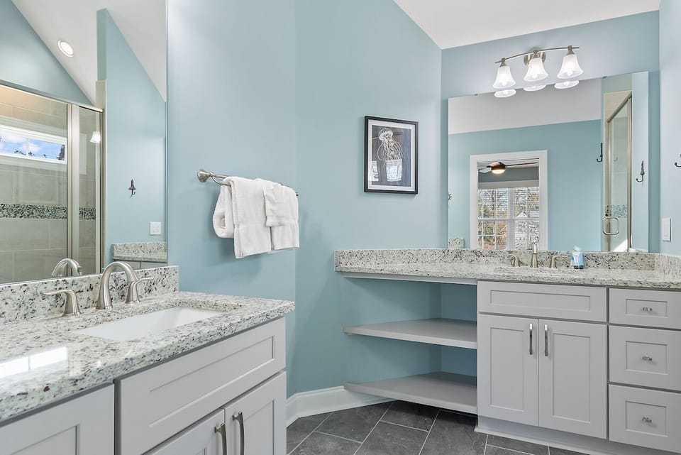 Unwind in this serene spa-like bathroom with dual vanities, granite countertops, and calming blue walls that create your perfect morning routine.