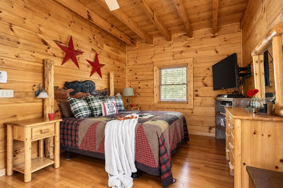 The room has nightstands on both sides, a TV, and a wood dresser with a mirror. It's a comfy space for a couple to rest after a day in the mountains.