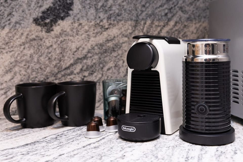 A Nespresso machine with milk frother, capsules, and matte black mugs sit ready on the marble benchtop — so guests can enjoy a proper coffee from the moment they arrive.