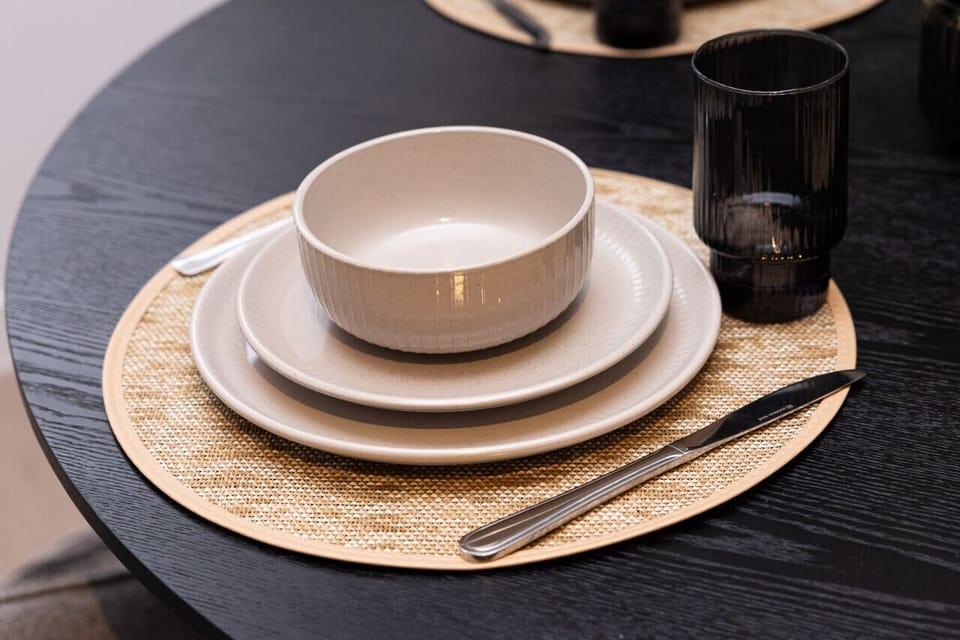 A close-up of the dining place setting — ribbed stoneware bowl and plates on a woven placemat with smoked glassware and polished cutlery, showing the quality tableware provided for guests.